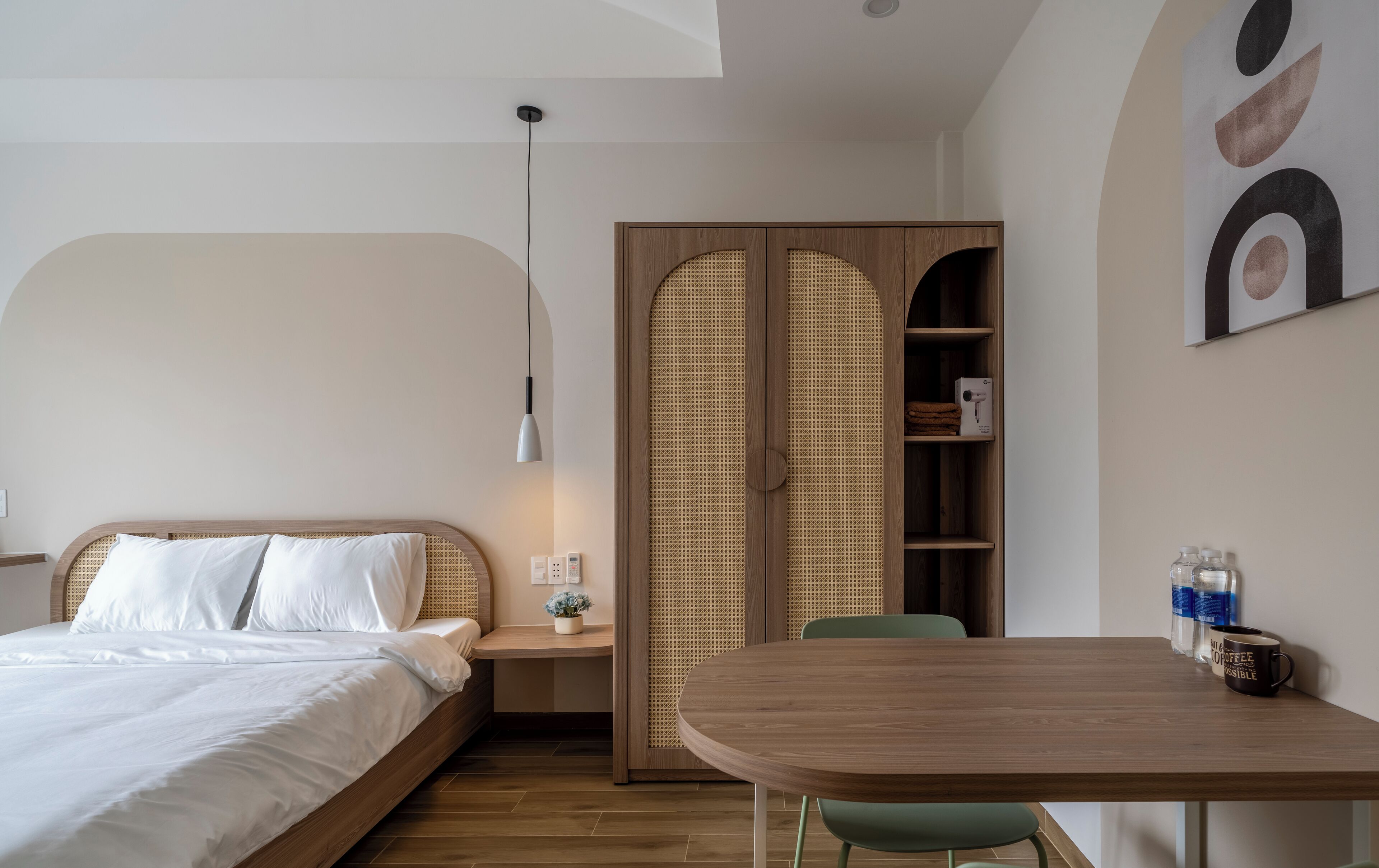 A modern bedroom with a bed, bedside table, lamp, and a wooden wardrobe with a woven door.