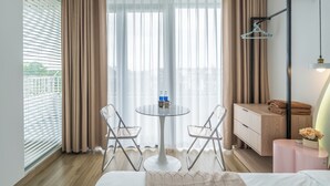 A hotel room with a bed, a small round table with chairs, a bedside table with a lamp, a wardrobe, and a window with curtains. - Ti Tach Homestay in Eco Garden Hue (Hue)
