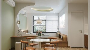 A modern dining area with a round table, four chairs, a bench, and a large window with blinds. - Ti Tach Homestay in Eco Garden Hue (Hue)