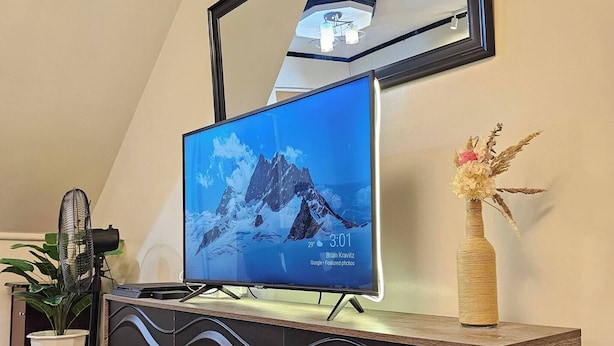 A modern living room with a flat-screen TV on a wooden console, a large mirror above it, and a potted plant beside the TV. - Cozy Biñan Getaway - Entire House for Rent (Biñan City)