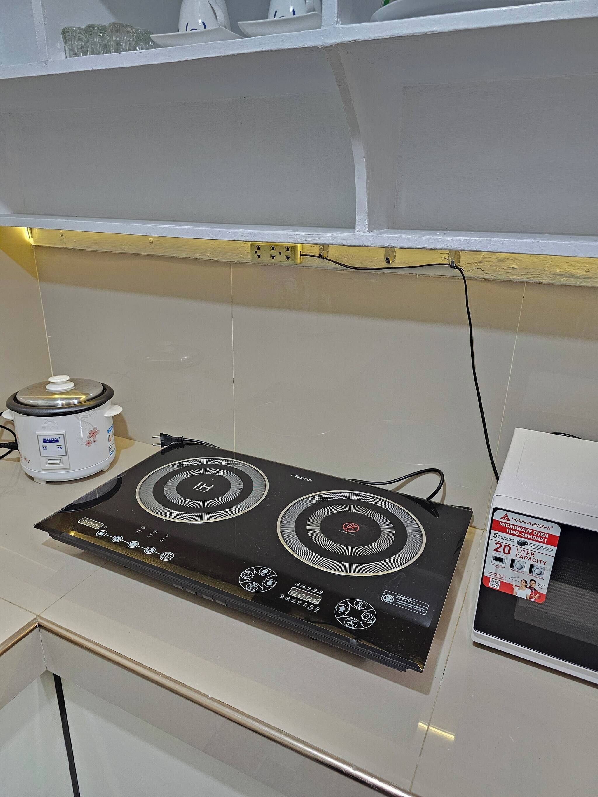 Una cocina con una placa de inducción negra, una olla de cocción lenta blanca y un horno microondas.