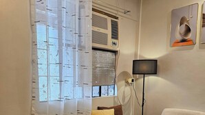 A living room with a sofa, a coffee table, a lamp, and a window with a curtain. - Cozy Biñan Getaway - Entire House for Rent (Biñan City)