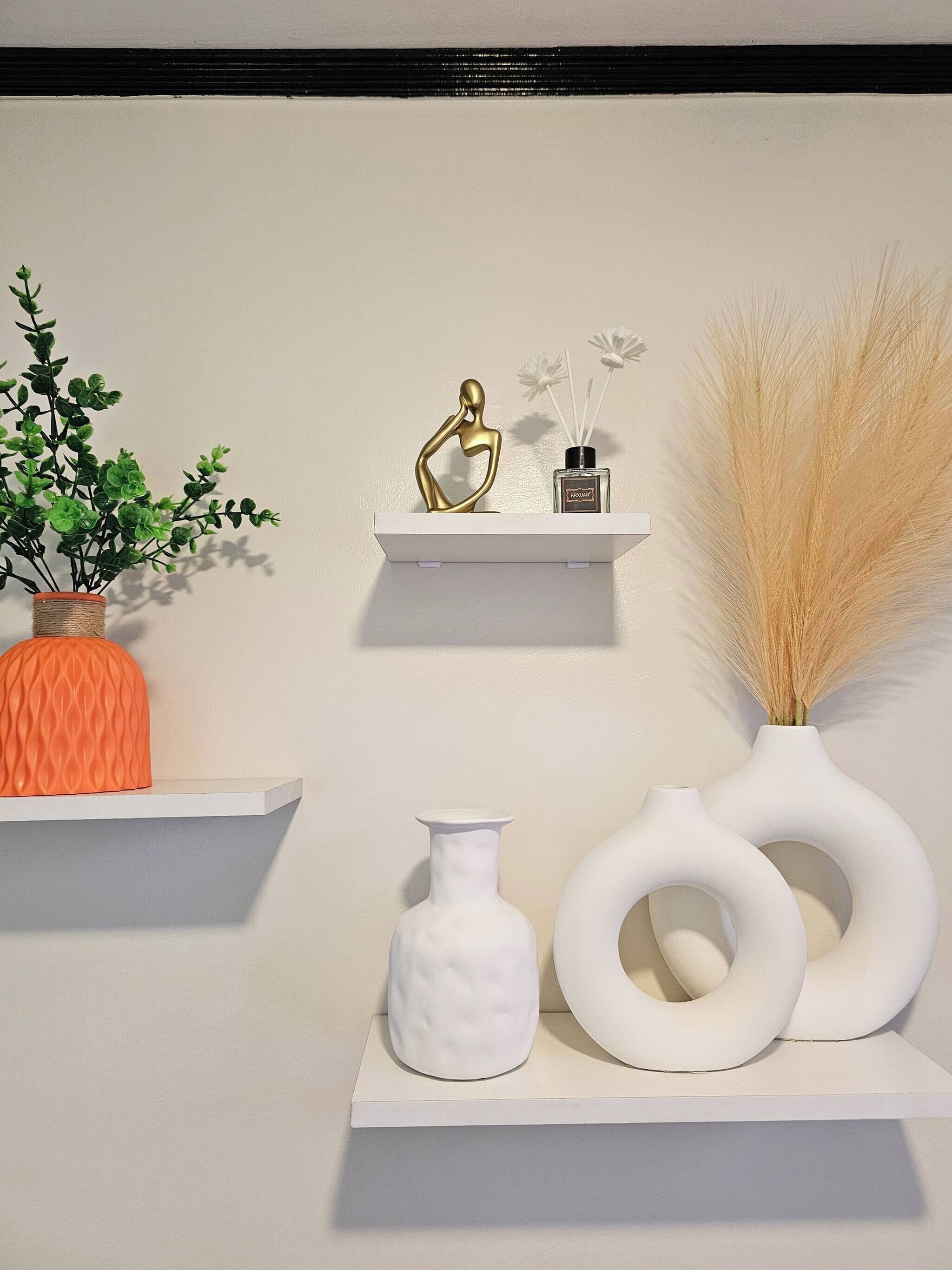 A wall with three white shelves displaying various decorative items.
