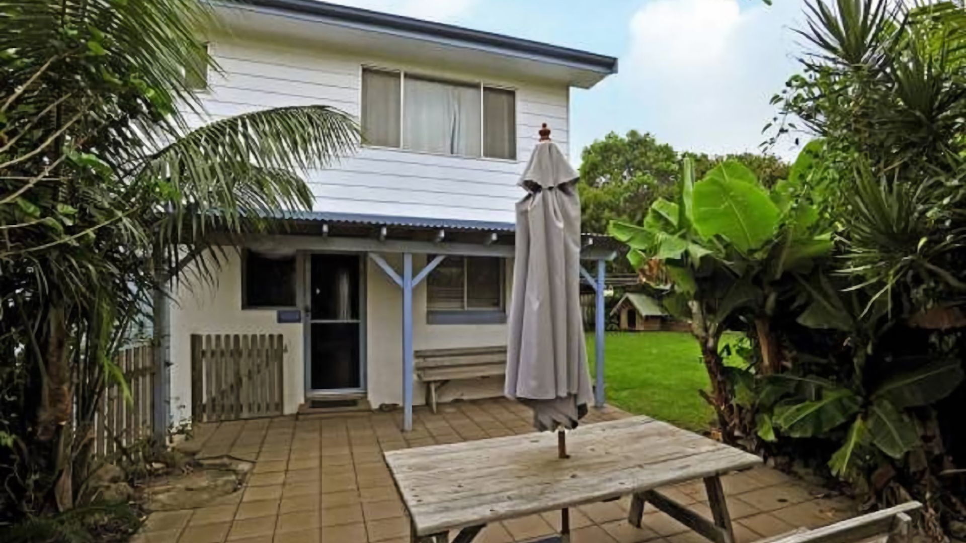 A house with a covered patio, a wooden table, and a bench.