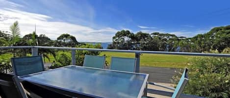 A balcony with a glass table and chairs, overlooking a grassy area and trees.