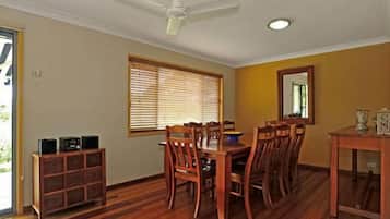 A dining area with a wooden table and chairs, a ceiling fan, and a window with blinds.