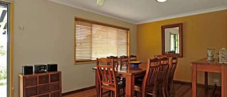 Comedor con mesa y sillas de madera, ventilador de techo y ventana con persianas.