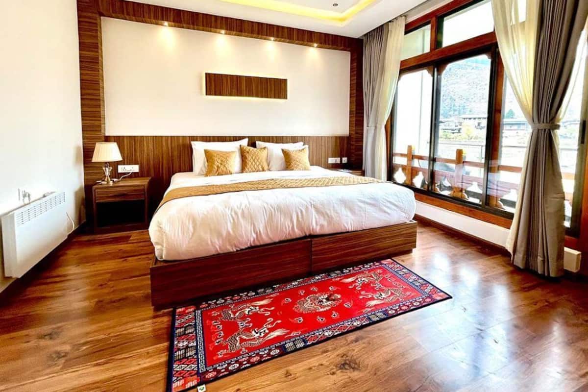 A modern bedroom with a large bed, wooden paneling, a red patterned rug, and a view through a large window.