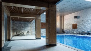An indoor swimming pool with stone walls and wooden beams, a seating area with chairs, and a view of the pool. - Aivazovsky (Gyumri)
