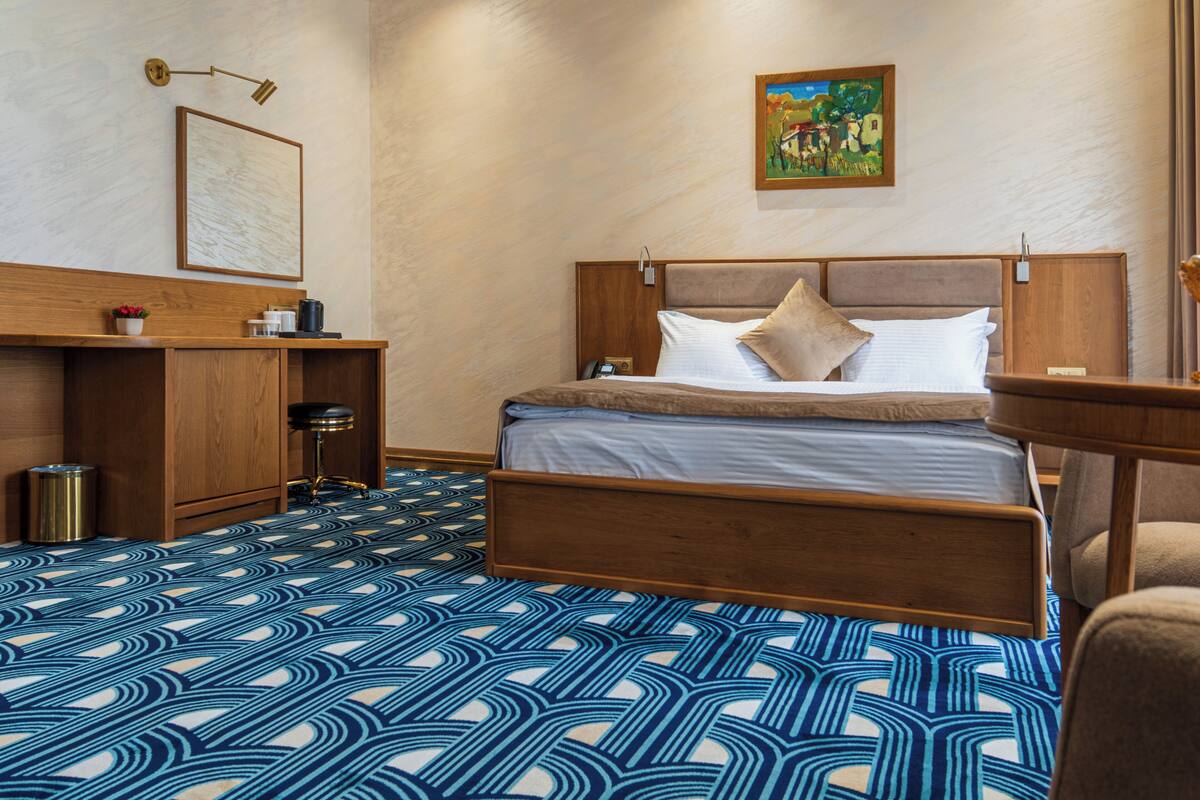 Une chambre d’hôtel avec un lit, un bureau, une poubelle et un tableau au mur.