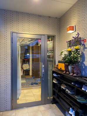 A modern hotel entrance with a glass door, a brick-patterned wall, and a shoe display. - Tokyo guest house 2020 (荒川区)