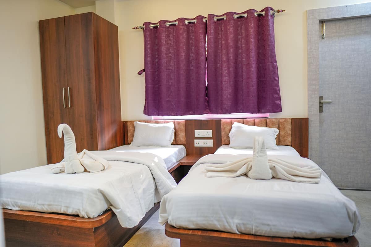 A hotel room with two beds, wooden wardrobe, purple curtains, and a door.