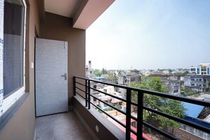 A balcony with a metal railing, a door, and a view of a residential area with various buildings. - Shivpriya Palace (Deoghar)