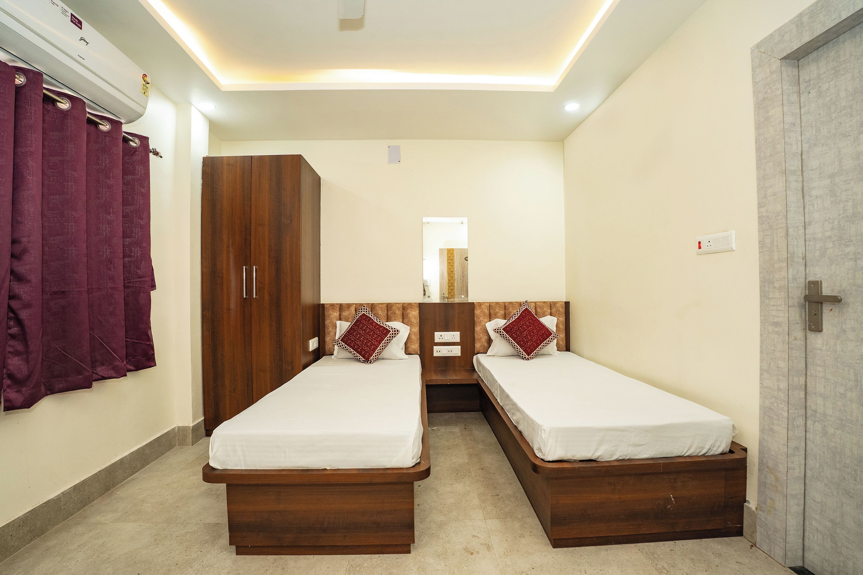 A bedroom with two single beds, a wardrobe, a mirror, and a door.