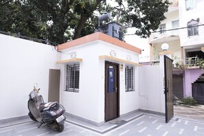 A white building with a brown door and windows, a scooter parked in front, and a gate to the right. - Shivpriya Palace (Deoghar)