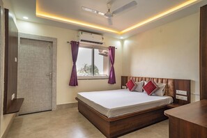 Ein Schlafzimmer mit einem Bett, einem Deckenventilator, einer Klimaanlage, einem Fenster mit Vorhängen und einer Tür.