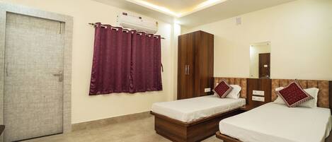 A hotel room with two single beds, a wardrobe, a ceiling fan, an air conditioning unit, and a door.