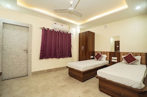 A hotel room with two single beds, a wardrobe, a ceiling fan, an air conditioning unit, and a door.
