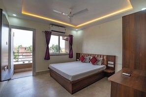 A bedroom with a bed, a ceiling fan, an air conditioning unit, a window with curtains, and a view of the outside. - Shivpriya Palace (Deoghar)