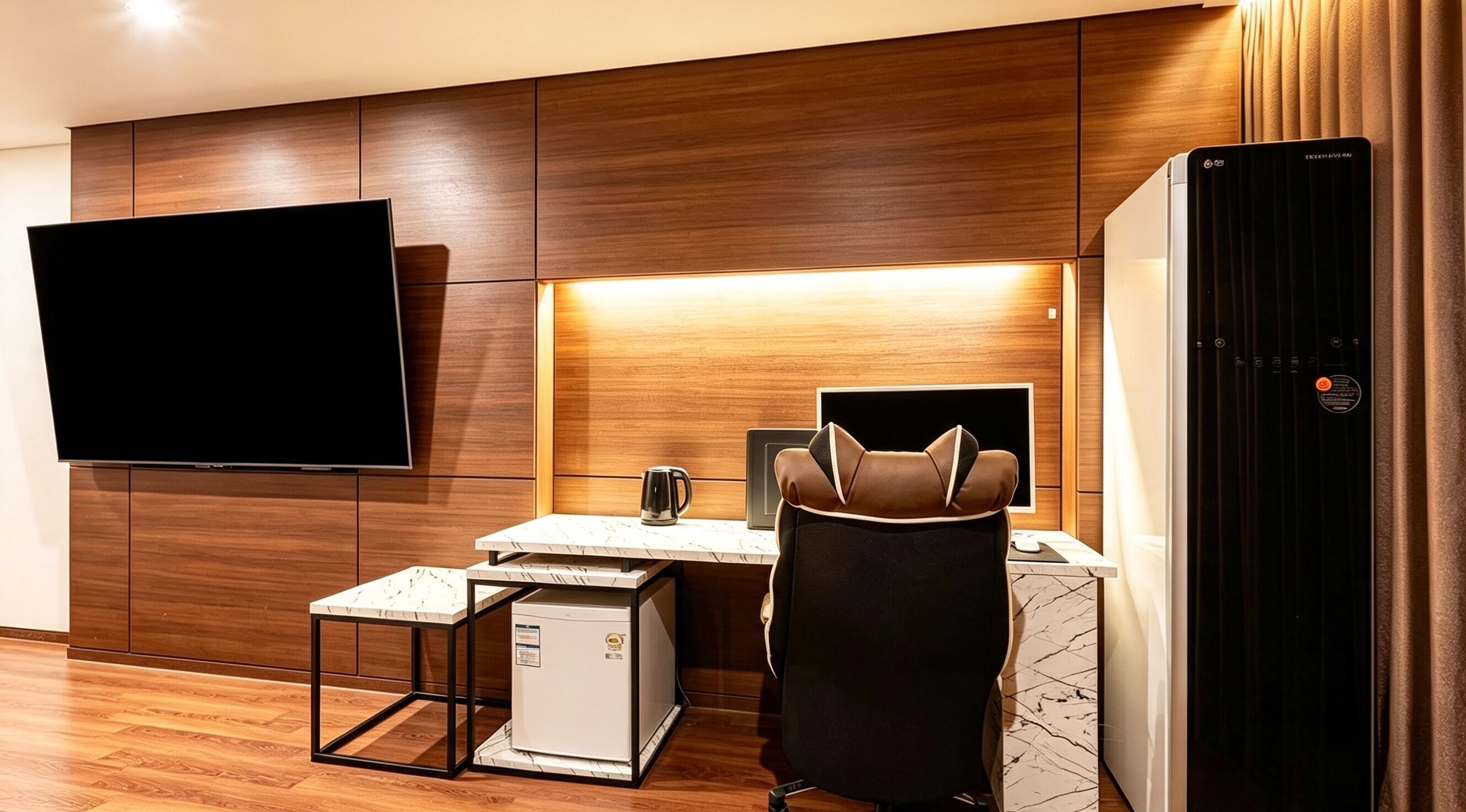Une chambre d’hôtel moderne équipée d’un téléviseur à écran plat fixé au mur, d’une petite kitchenette, d’un coin salon avec un fauteuil et d’un réfrigérateur.