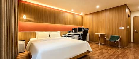 Een hotelkamer met een groot bed, een bureau met een computer, een stoel, een klein tafeltje en een groene stoel.