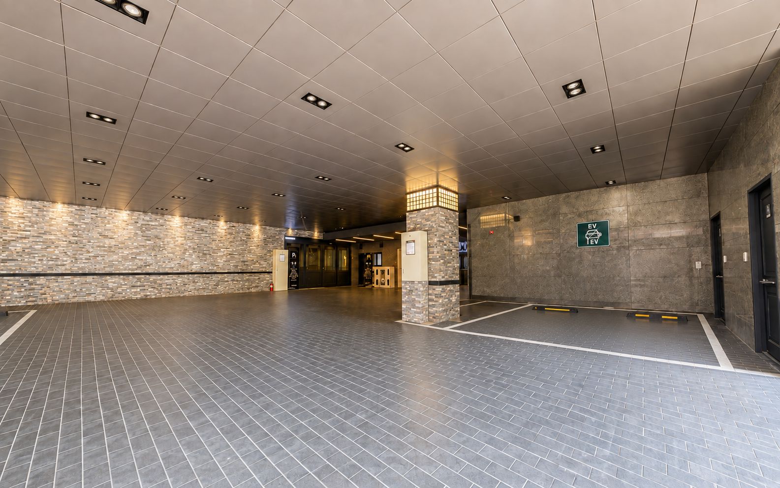 A spacious indoor area with a tiled floor, a stone wall, and a sign indicating an EV charging station.