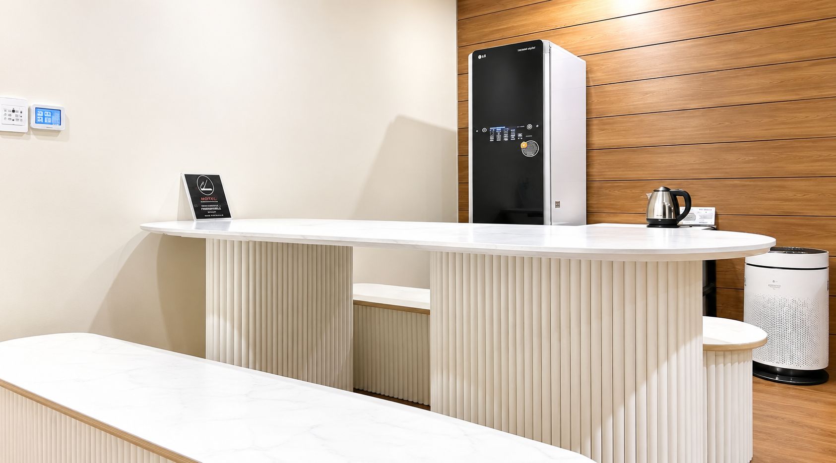 Un'accoglienza moderna con una reception bianca, un purificatore d'aria bianco e nero e un bollitore sul bancone.