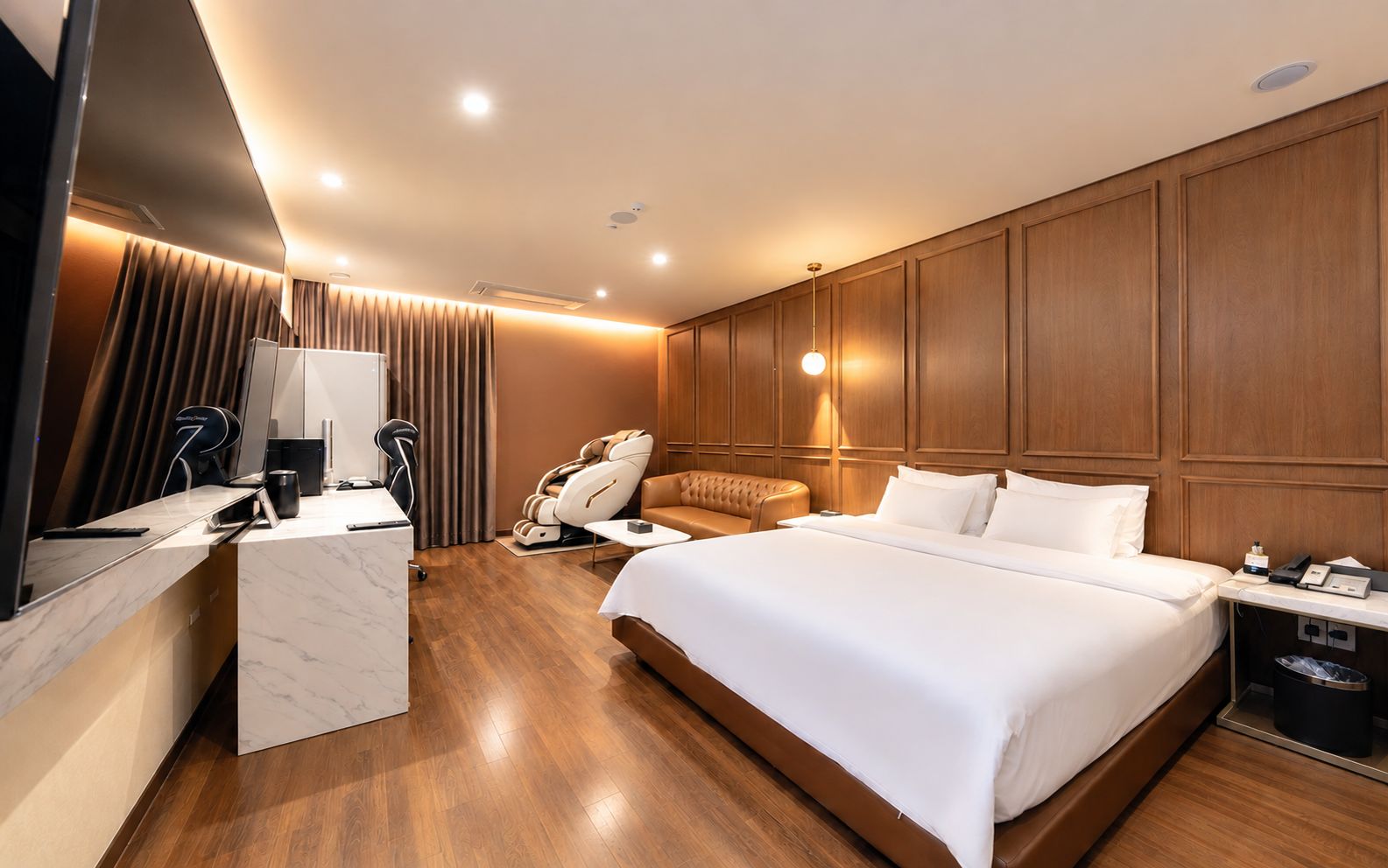 Una camera d'albergo con un letto, poltrona massaggiante, scrivania e televisore.