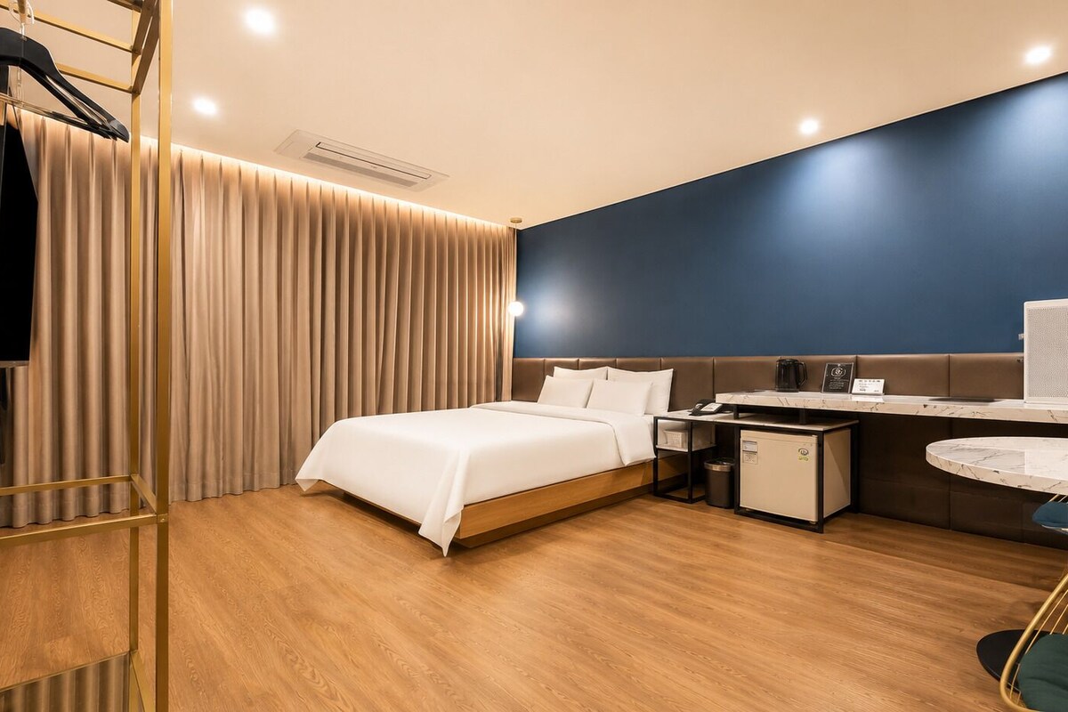 Habitación de hotel con cama, escritorio, refrigerador pequeño, cafetera y mesa redonda.