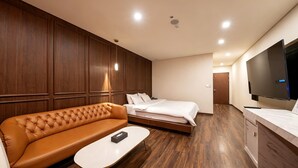 Habitación de hotel con sofá de cuero marrón, cama individual, una mesita pequeña y televisor montado en la pared.