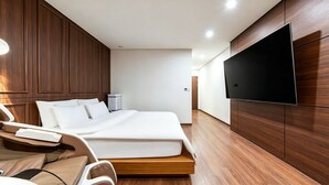 Una habitación de hotel moderna con una cama grande, un televisor de pantalla plana montado en la pared y suelo de madera.