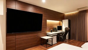 Habitación de hotel moderna con una televisión de pantalla plana grande, un escritorio con una computadora, una silla y un refrigerador pequeño.