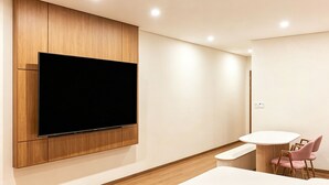 Una habitación moderna con televisor montado, una mesa redonda con sillas y piso de madera.
