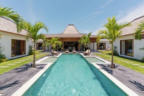 Een modern resort met een centraal gelegen zwembad, palmbomen en een overdekte buitenruimte met zitplaatsen.