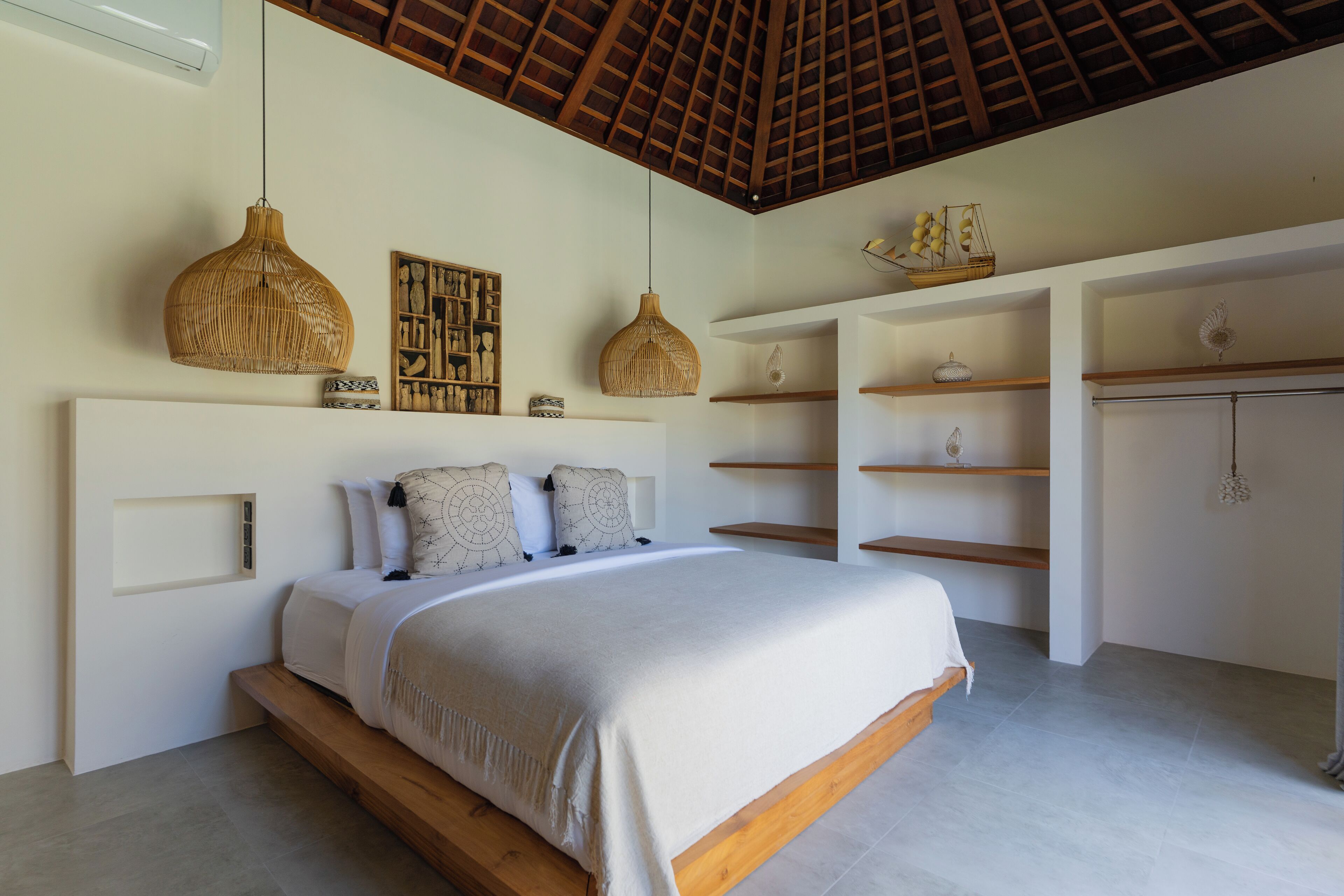 A bedroom with a large bed, wooden headboard, hanging rattan lamps, and built-in shelves.