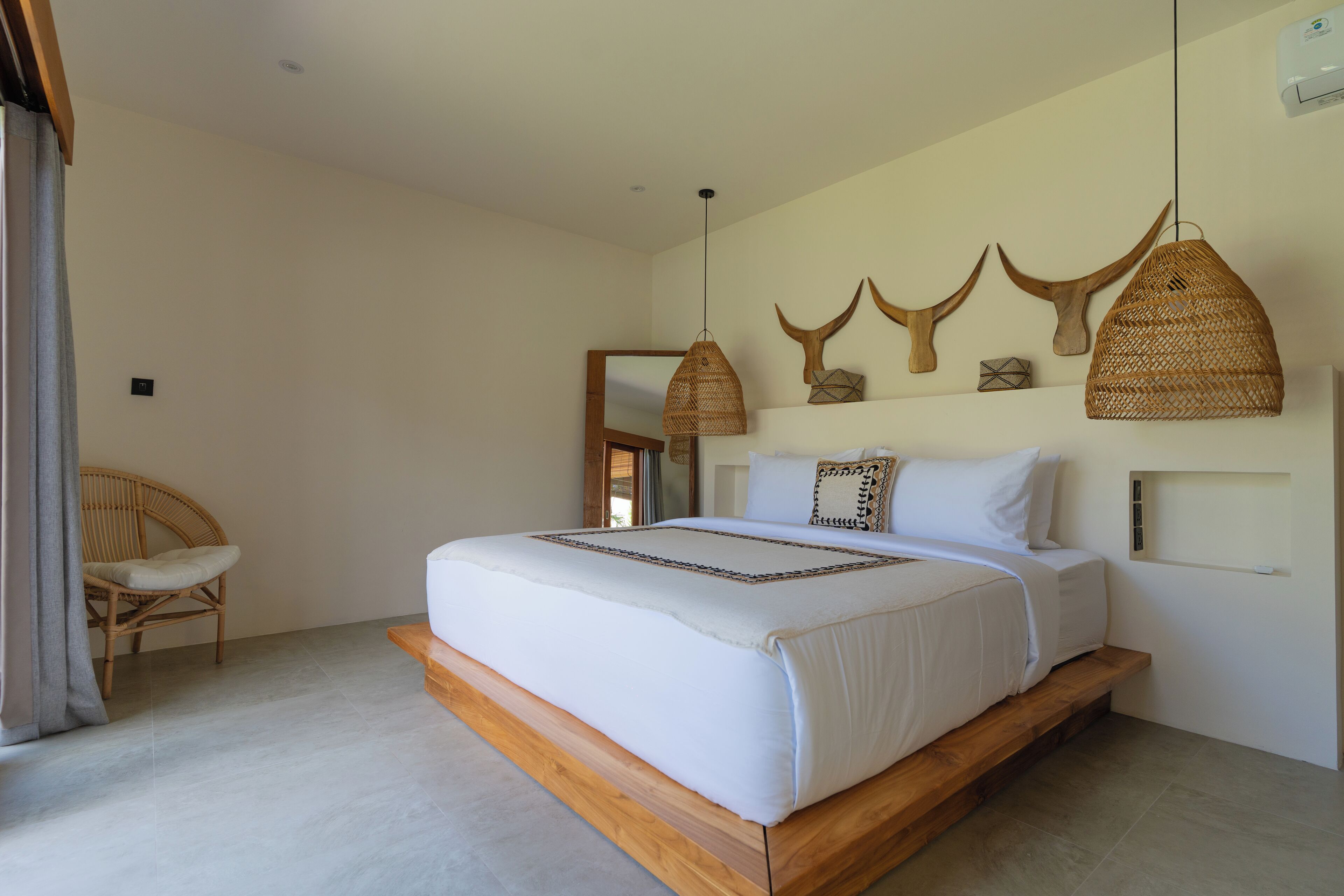 A bedroom with a large bed, a wooden platform, a wicker hanging light, and wall-mounted decor.