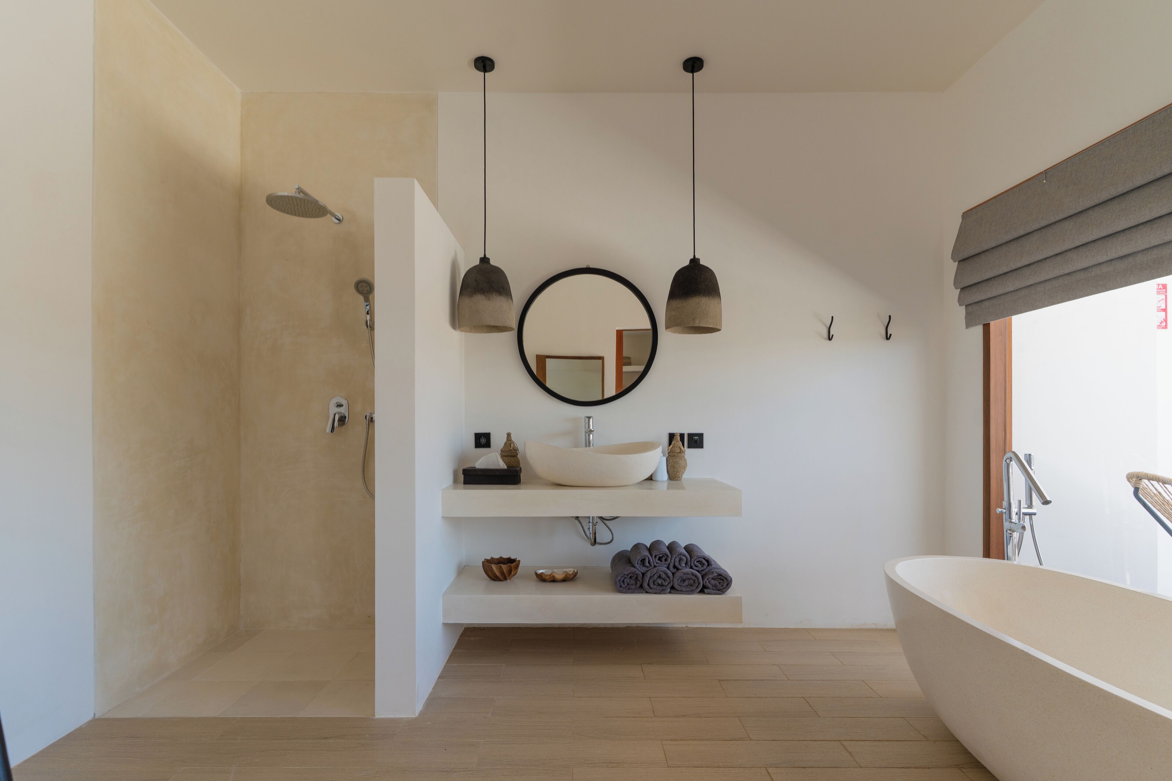 A modern bathroom with a freestanding bathtub, a round mirror, pendant lights, and a shower area.