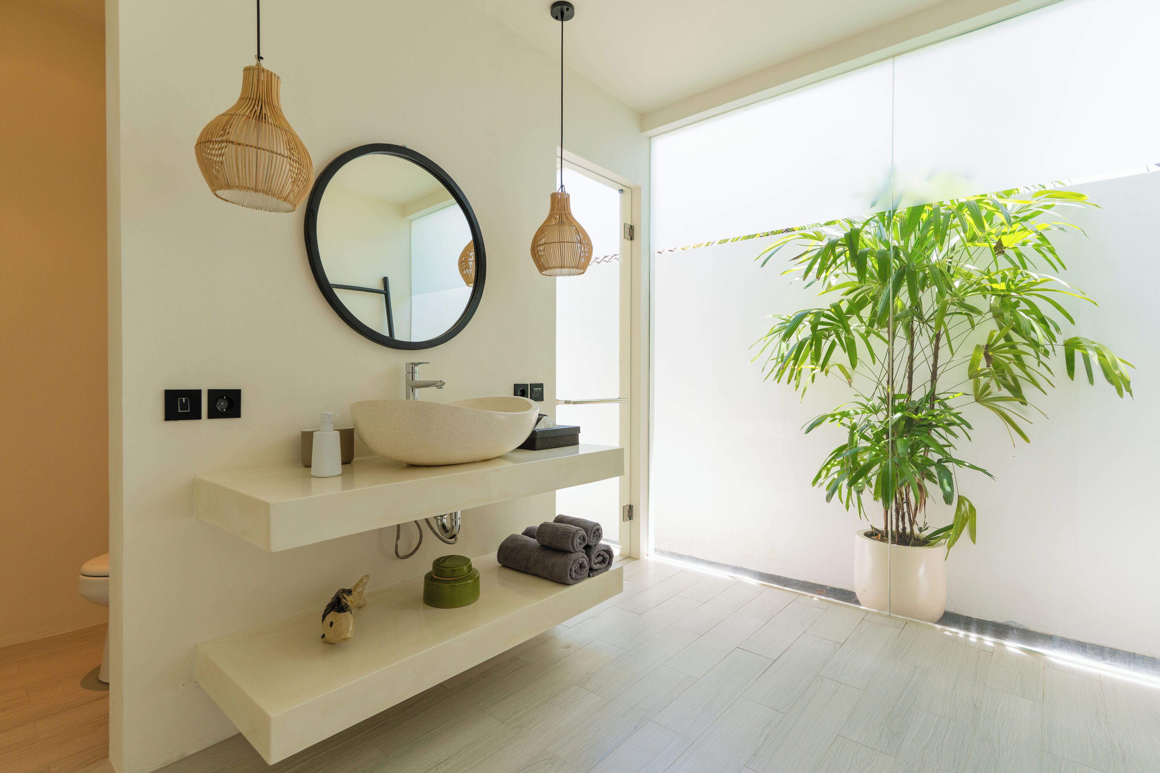 A modern bathroom with a large mirror, white shelves, a sink, and a potted plant.