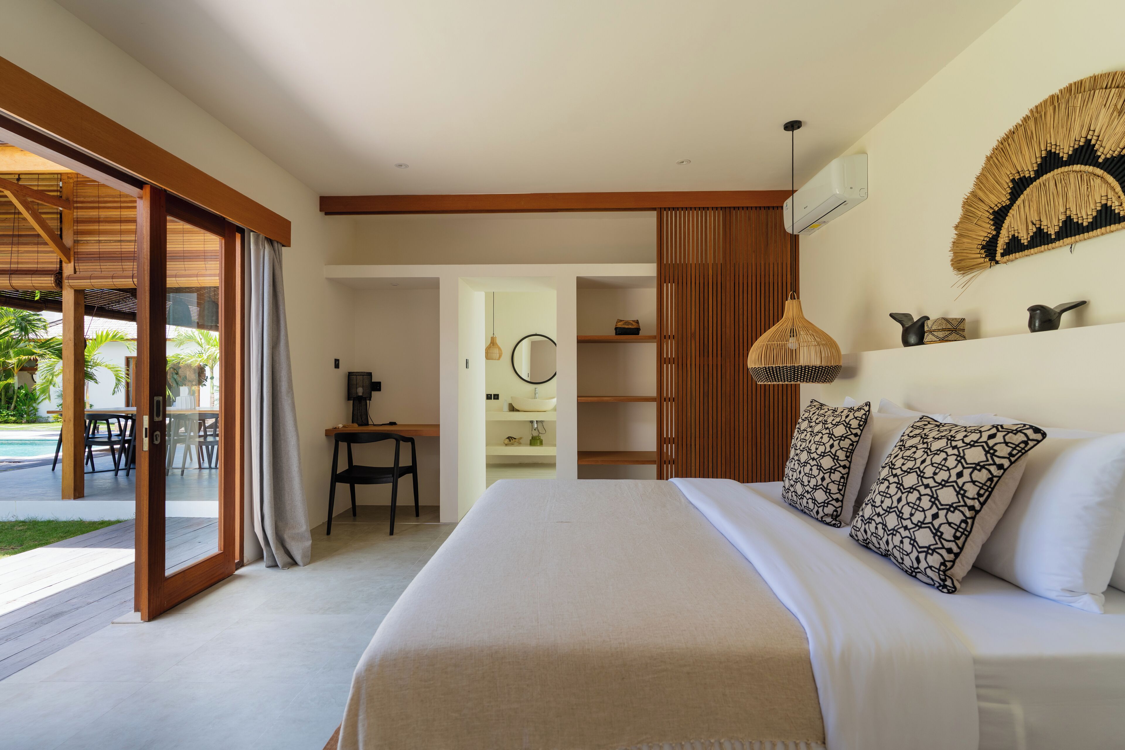 A modern bedroom with a large bed, a desk, and a bathroom visible through an open door.