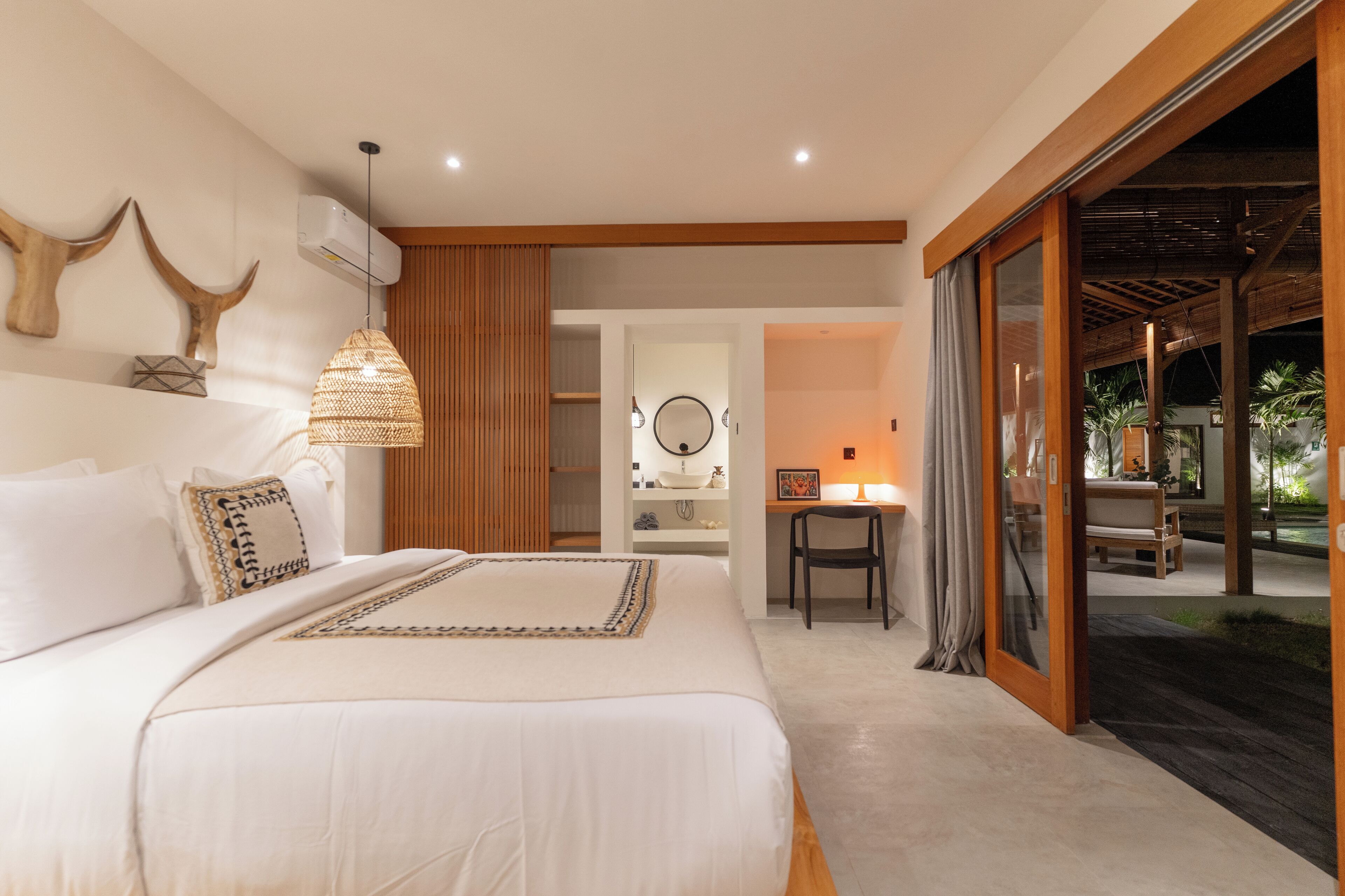 A modern bedroom with a large bed, a desk, and a view of the outdoors.