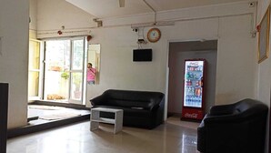 A spacious room with a black leather sofa, a small white table, a black armchair, a ceiling fan, a wall-mounted TV, and a Coca-Cola refrigerator. - Hotel Saubhagya Elite (Nashik)