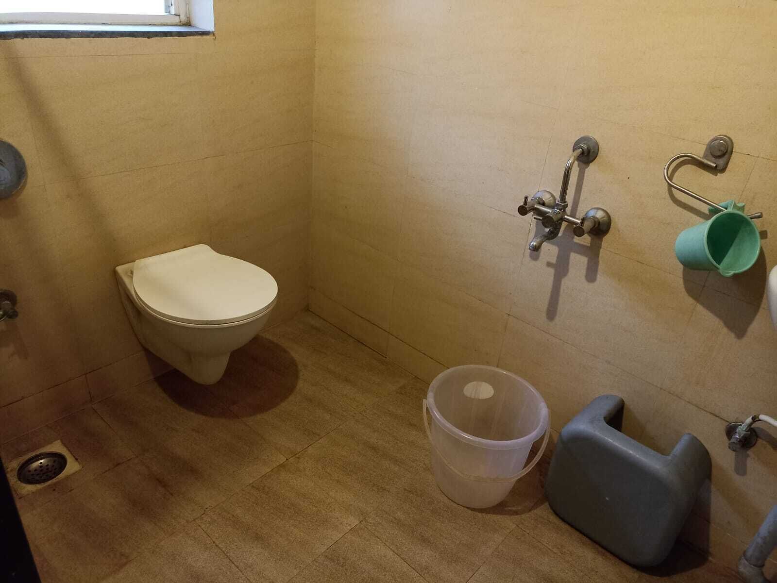 A small bathroom with a toilet, a wall-mounted faucet, a trash bin, and a plastic container.