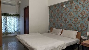 A bedroom with a bed, a window with floral curtains, a wall with a floral wallpaper pattern, and a door. - Hotel Saubhagya Elite (Nashik)