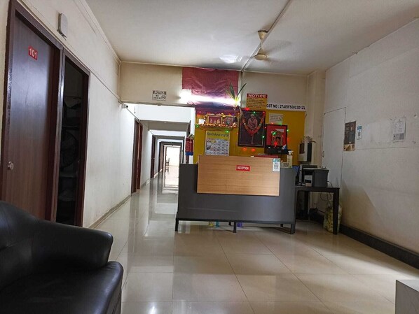 A reception area with a reception desk, a ceiling fan, and a corridor leading to other rooms. - Hotel Saubhagya Elite (Nashik)