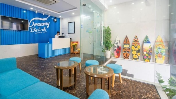Un espace d’accueil avec un comptoir bleu, une réceptionniste et un mur de verre où sont exposées des planches de surf.