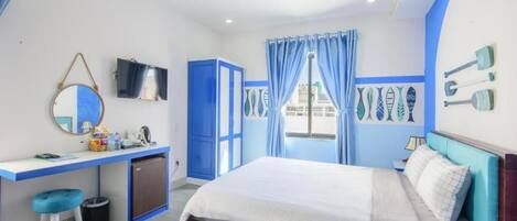 A bedroom with a bed, a desk, a chair, a TV, and a window with curtains.