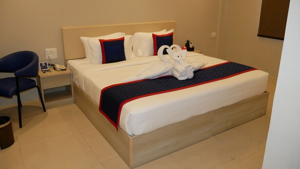 A hotel room with a bed, a chair, a nightstand, and a wall-mounted phone. - Surendra Landmark By Spree Hotels (Bhopal)