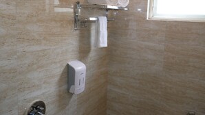 A bathroom with marble walls, a towel rack with rolled towels, a toilet paper dispenser, and a window. - Surendra Landmark By Spree Hotels (Bhopal)