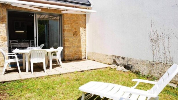 Un patio con una mesa y sillas, una silla lounge blanca y un edificio de piedra con puerta de vidrio.