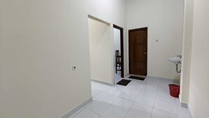 Un pasillo con pisos de baldosas blancas, una puerta de madera, un lavamanos blanco y una cesta roja.